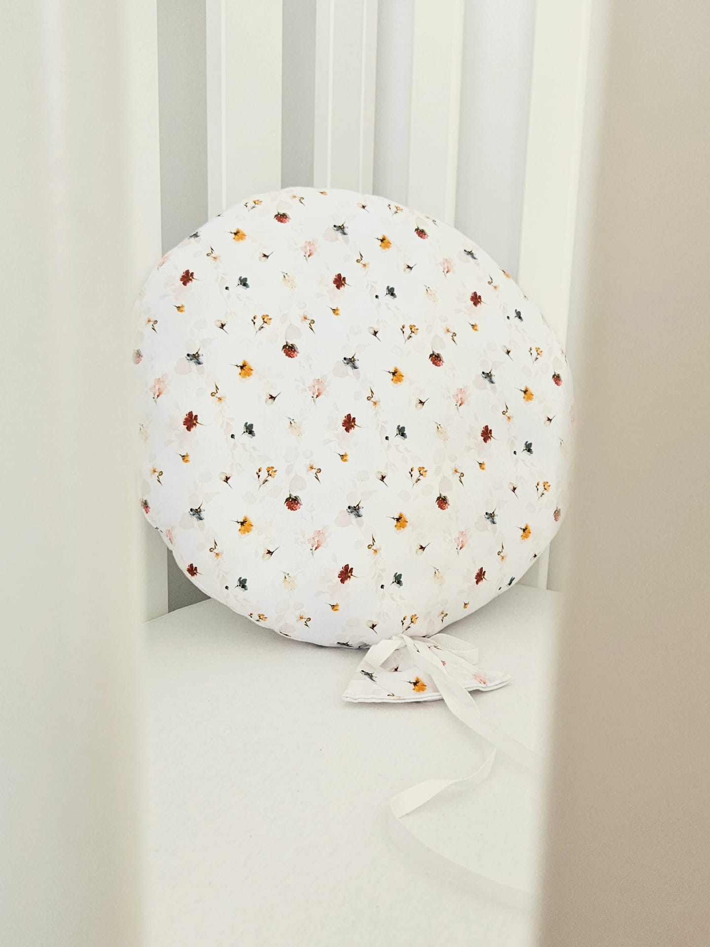 Balon decorativ textil din bumbac alb cu imprimeu floral si panglici, asezat pe un patut pentru copii.