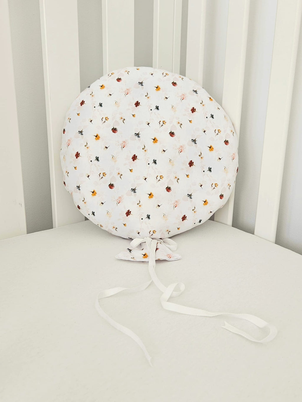 Balon decorativ textil din bumbac alb cu imprimeu floral si panglici, asezat pe un patut pentru copii.