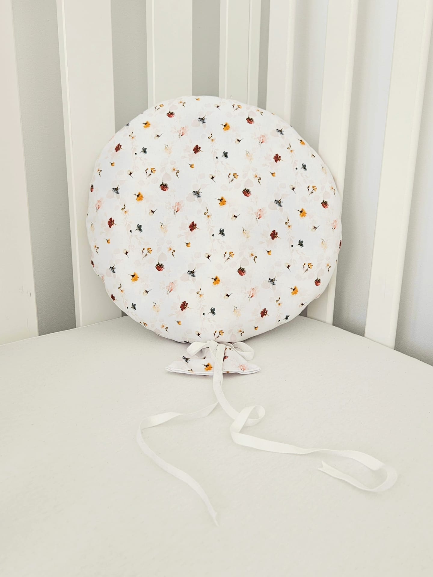 Balon decorativ textil din bumbac alb cu imprimeu floral si panglici, asezat pe un patut pentru copii.