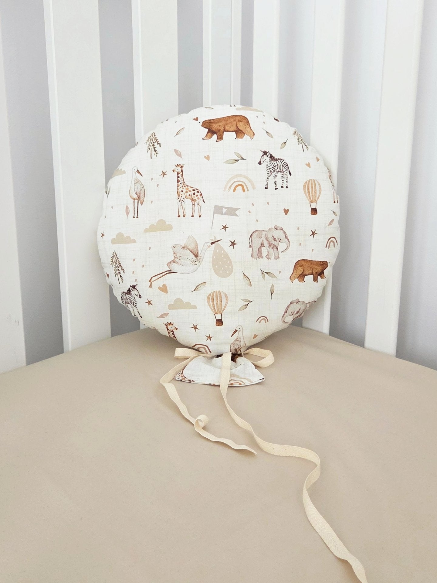Balon decorativ textil din bumbac alb cu imprimeu floral si panglici, asezat pe un patut pentru copii.